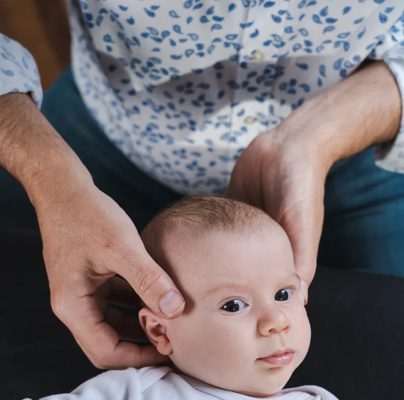 Mãos de um terapeuta apoiadas com delicadeza na cabeça de um bebê durante a avaliação